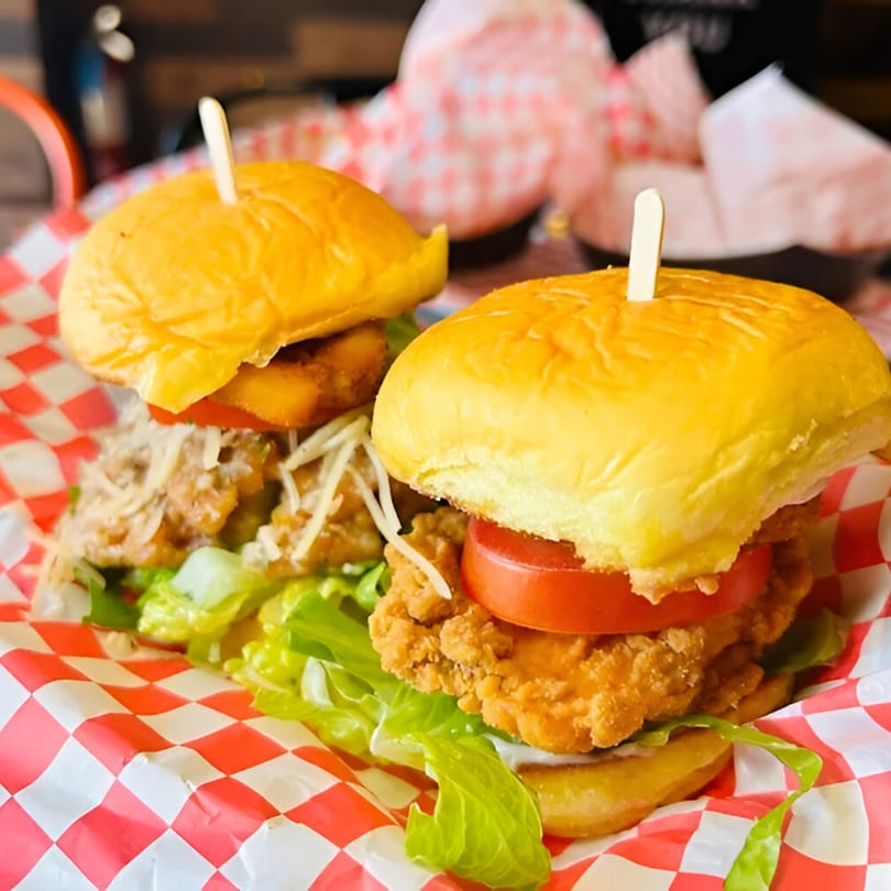 Two Chick Wings and Things chicken sliders with lettuce and tomato on red and white checkered paper.