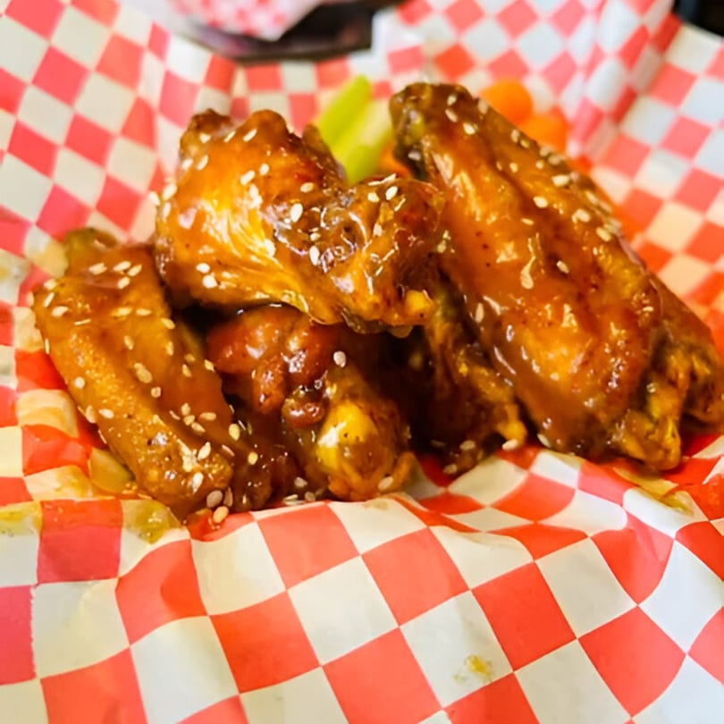 Sweet and sticky Chick Wings and Things wings, topped with sesame seeds, served in a red and white checkered basket.