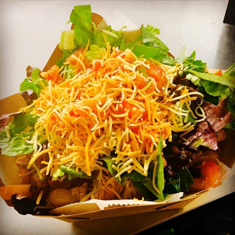 A close-up of a Chick Wings and Things salad with shredded cheese, lettuce, and tomatoes.